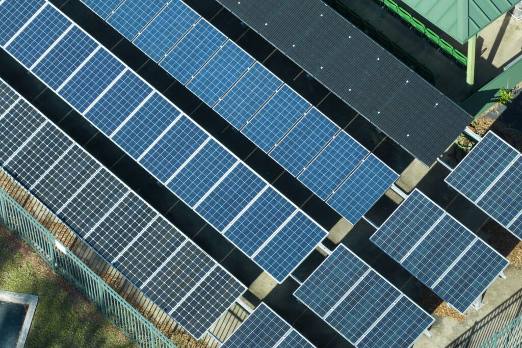 Aerial view of blue solar photovoltaic panels mounted on fenced backyard for producing